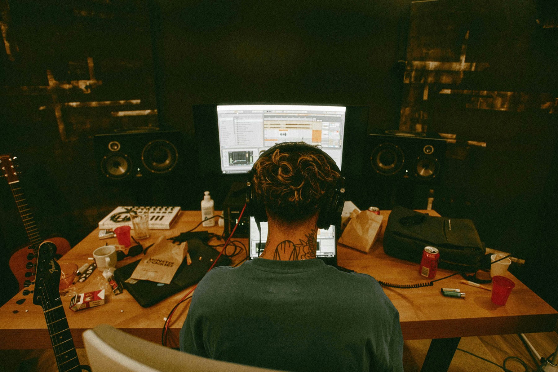 A songwriter at a home studio workstation, headphones on, guitar within reach — the moment the song is finished.